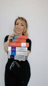 Katrina, cosmetic injector at Third Eye Beauty Lounge, holding a stack of Juvederm dermal filler boxes with a confident smile.